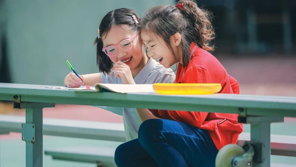 two smiling young female students working on homework outside chengdu international school elementary