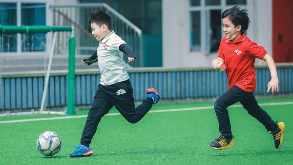 two young male students playing soccer about chengdu international school playing field